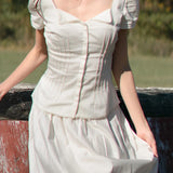 Woman wearing a white dress with puffed sleeves against a natural background