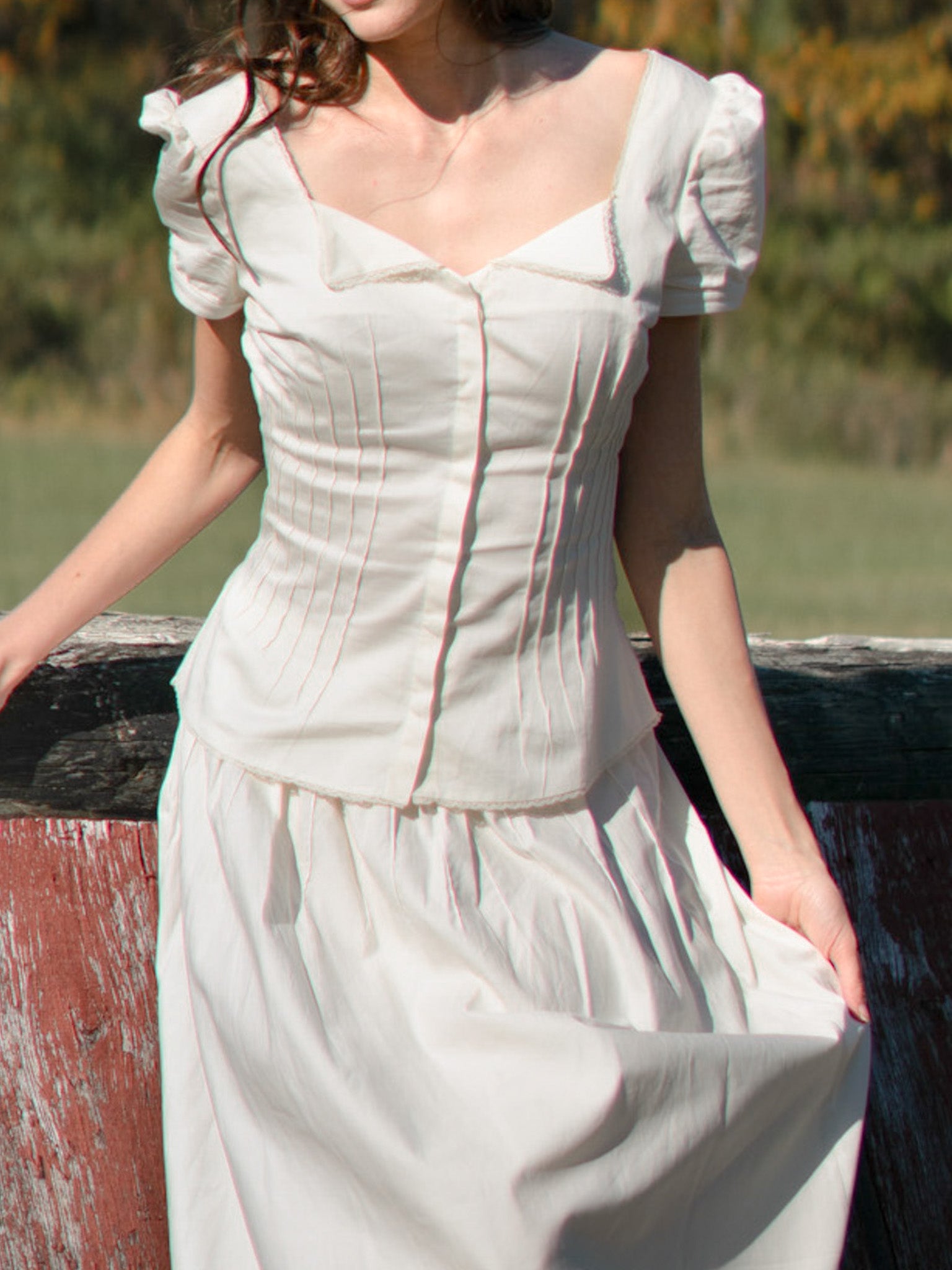 Woman wearing a white dress with puffed sleeves against a natural background